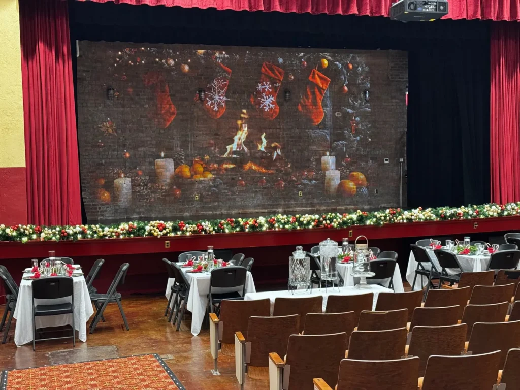 Dinner tables set in front of the stage, with a fireplace scene on the screen and red curtains