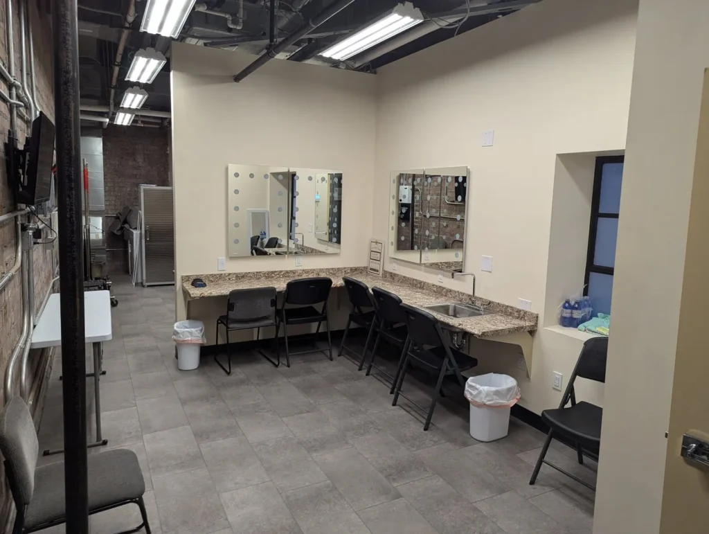 A dressing room with lit mirrors, a long counter and chairs