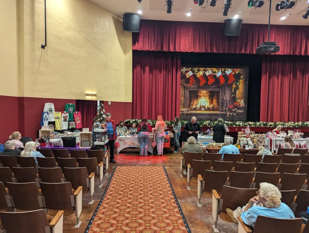 Holiday market stalls in the auditorium, with visitors in the seats and a fireplace scene on stage