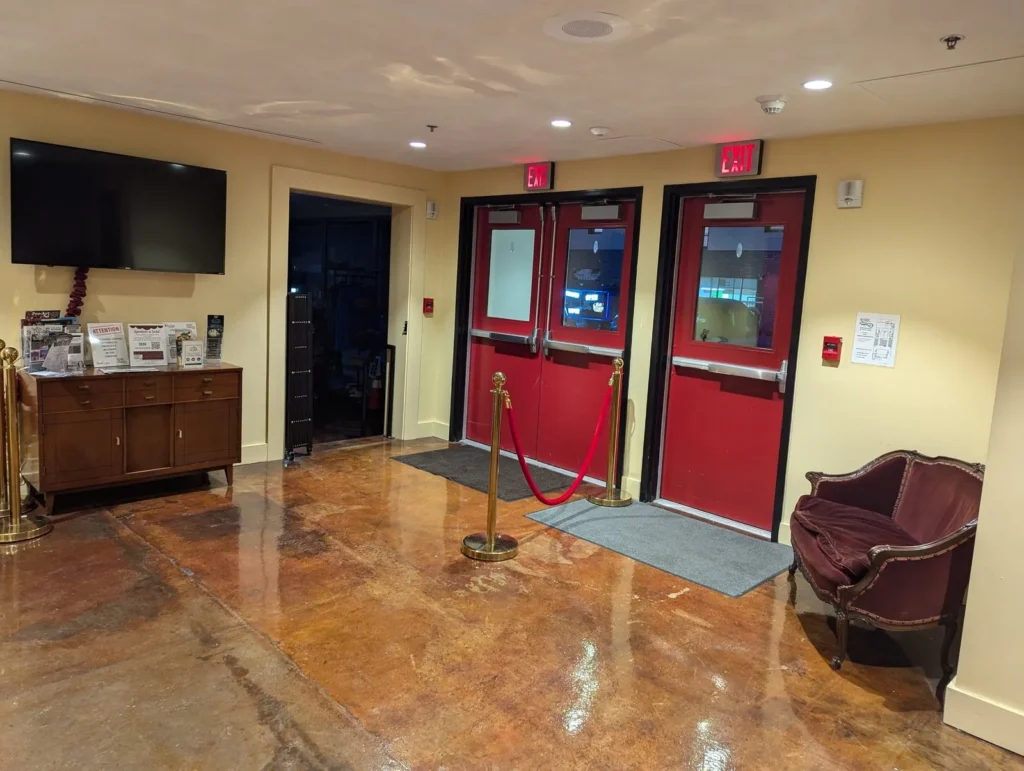 The Lyric's lobby: red doors into the auditorium, a soft chair and a television on the wall