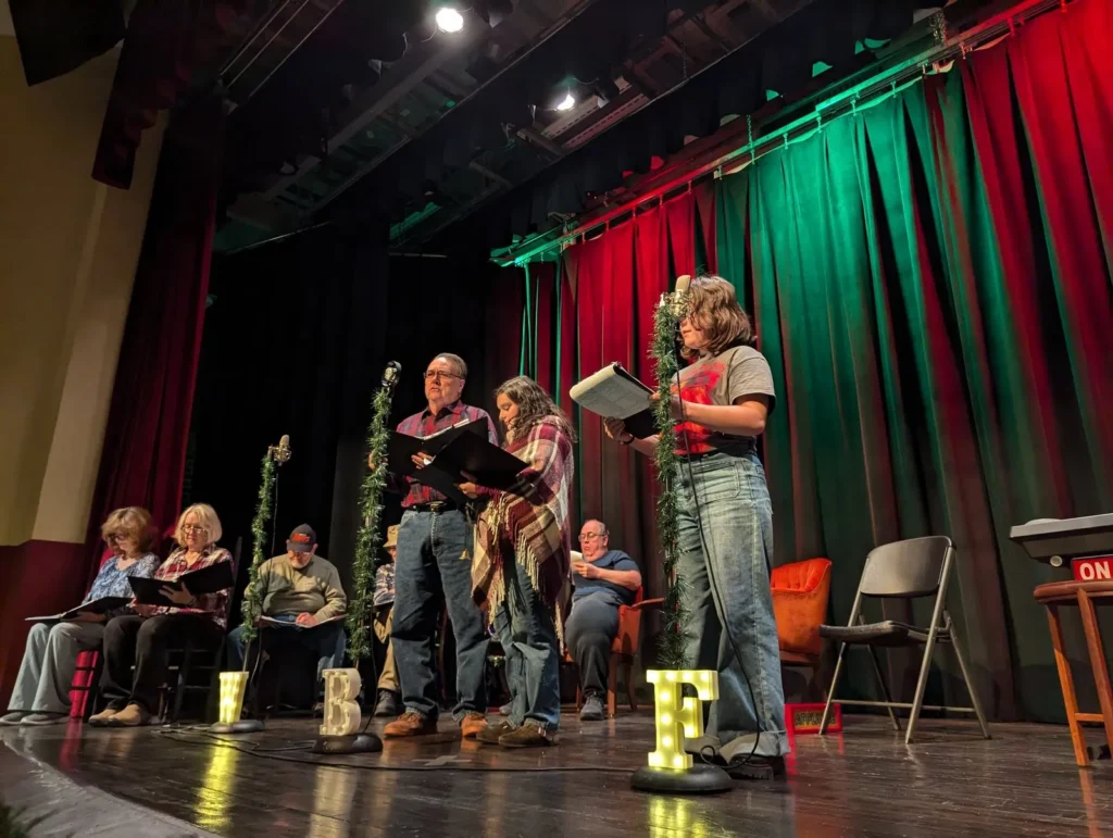 Performers at microphones on the Lyric stage, between red and green curtains, at a holiday radio-style show